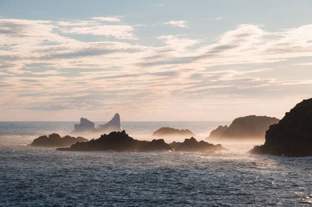 Iceberg drifts past a misty rocky coastline in Newfoundland Twillingate, Newfoundland and Labrador, Canada CR_DOHO26070204-2072542-01