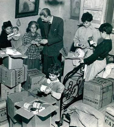 RECORD DATE NOT STATED Photo of humanitarian aid distribution in Italy. Photograph of Marshall Aid packages arriving in Italy in 1948, depicting a group of people, including children and adults, gathered in a room filled with boxes labelled CARE. They are distributing and examining canned goods and other supplies, illustrating the humanitarian aid efforts in post-war Europe. 1948. Editorial use only. All other uses to be cleared with the copyright owner (World History Archive), in advance., WHA_298_0101.jpg, Marshall Aid; Italy; CARE packages; Post-war Europe; 1948; Humanitarian aid; European Recovery Program; Cold War; Economic recovery; Post-WWII reconstruction; Foreign aid; US foreign policy; Food relief; European history; Cold War his Copyright: xWorldxHistoryxArchivex