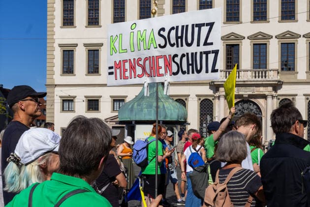 Augsburg, Bavaria, Germany - July 10, 2026: Demonstration by the climate justice movement Fridays for Future and Greenpeace in Augsburg. Under the nationwide slogan Protect the climate, fire the rich, the activists are protesting, among other things, against current gas infrastructure policy and planned gas drilling in Bavaria. Demonstrators holding a sign that reads: Climate protection is human protection *** Demonstration der Klimaschutzbewegung Fridays for Future und GREENPEACE in Augsburg. Unter dem bundesweiten Motto: Klima schützen, Reiche entlassen, protestieren die Aktivisten unter anderem gegen die aktuelle Gas-Infrastrukturpolitik und geplante Gasbohrungen in Bayern. Demonstranten mit Plakat: Klimaschutz ist Mensche