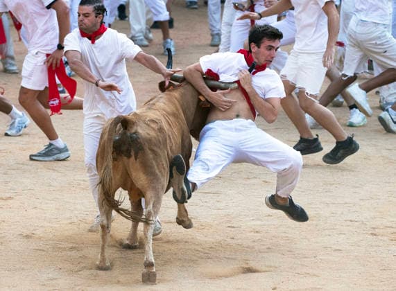 A reveler is hit by a wild cow with padded hors as he tries his luck and skill inn the bull ring following the fifth encierro , or running-of-the-bulls in the Fiesta de San Fermin and Feria del Toro in Pamplona, northern Spain, on Saturday July 11, 2026.  PAM20260711154 JimxHollander