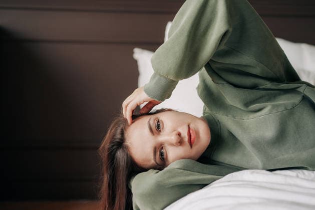 Junge Frau liegt auf einem Bett in einem grünen Pullover, entspannt und nachdenklich mit weichem natürlichem Licht. Young woman lies on a bed in a green sweater, relaxed and thoughtful with soft natural light. (License=RF) ,model released, Symbolfoto Copyright: xZoonar.com TITOVAxILONAx 25277598 ,model released, Symbolfoto ,property released