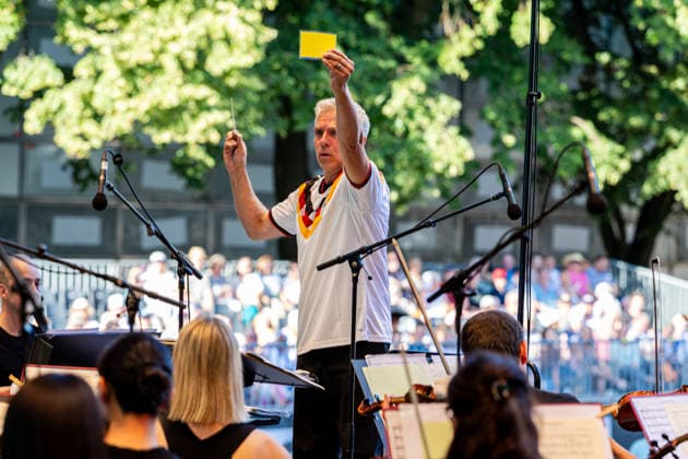 Klassik!Picknick mit dem Beethoven Orchester auf dem Kunst!Rasen Bonn Generalmusikdirektor Dirk KAFTAN im Deutschland Trikot zeigt einem öFalschspieler˜ die gelbe Karte - Das Beethoven Orchester Bonn unter der Leitung von Generalmusikdirektor Dirk KAFTAN beim Open-Air-Konzert KLASSIK!PICKNICK auf dem Kunst!Rasen Bonn-Gronau. Das Sommerprogramm steht unter dem Motto Fußball - passend zur WM 2026. Die Konzertreihe findet am Rande der Rheinaue am Bonner Rheinufer statt. Bonn Gronau Nordrhein-Westfalen Deutschland *** Classical Picnic with the Beethoven Orchestra on the Kunst Rasen in Bonn; General Music Director Dirk KAFTAN, wearing a Germany jersey, shows a cheater the yellow card; The Beethoven Orchestra Bonn, conducted by General M Copyright: xMarcxJohnx
