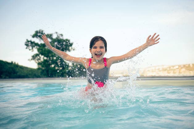 Ein kleines Mädchen im Badeanzug planscht fröhlich im Wasser, während es in einem Swimmingpool spielt, umgeben von viel Grün und einem strahlend blauen Himmel in einer sonnigen Umgebung im Freien Young girl in a swimsuit plays in a swimming pool, splashing water with her arms raised, with trees and a clear sky in the background (License=RF) ,model released, Symbolfoto Copyright: xZoonar.com DashaxPetrenkox 25282710 ,model released, Symbolfoto ,property released