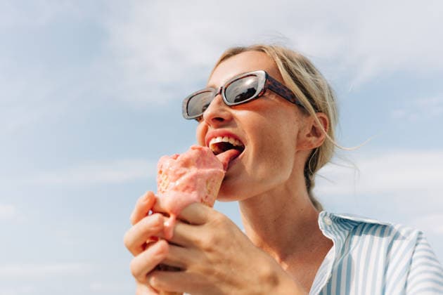 Eine Frau isst draußen eine schmelzende rosa Eistüte und lächelt dabei hinter ihrer Sonnenbrille an einem warmen, sonnigen Tag. A woman eats a melting pink ice cream cone outdoors, smiling in sunglasses on a warm sunny day. (License=RF) ,model released, Symbolfoto Copyright: xZoonar.com TITOVAxILONAx 25304741 ,model released, Symbolfoto ,property released