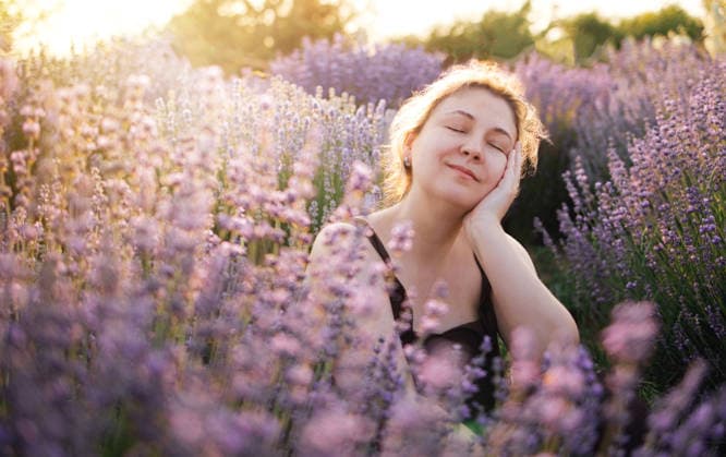 Eine Frau mit geschlossenen Augen genießt den Duft von Lavendelblüten in einem blühenden Feld bei Sonnenuntergang, umgeben von leuchtend violetten Blüten und sanftem Sonnenlicht Woman relaxes in a lavender field with closed eyes, surrounded by blooming purple flowers and warm sunlight filtering through the plants (License=RF) ,model released, Symbolfoto Copyright: xZoonar.com DashaxPetrenkox 25305471 ,model released, Symbolfoto ,property released
