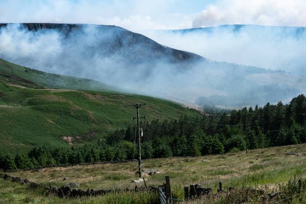 Moorland smoulders close to Dove Stone Reservoir in Greater Manchester on 13 July 2026. Greater Manchester Police have arrested a woman in connection with a large moorland fire at Dove Stone Reservoir in Greenfield. The blaze, burning since Saturday, is under active investigation, with officers following leads regarding reports of fireworks nearby. The 20-year-old suspect remains in custody as the cause of the fire is yet to be officially determined. Oldham Greater Manchester England Dovestone Reservoir  Copyright: xMattxWilkinsonx
