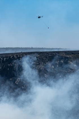 A helicopter carries water over smouldering moorland close to Dove Stone Reservoir in Greater Manchester on 13 July 2026. Greater Manchester Police have arrested a woman in connection with a large moorland fire at Dove Stone Reservoir in Greenfield. The blaze, burning since Saturday, is under active investigation, with officers following leads regarding reports of fireworks nearby. The 20-year-old suspect remains in custody as the cause of the fire is yet to be officially determined. Oldham Greater Manchester England Dovestone Reservoir  Copyright: xMattxWilkinsonx