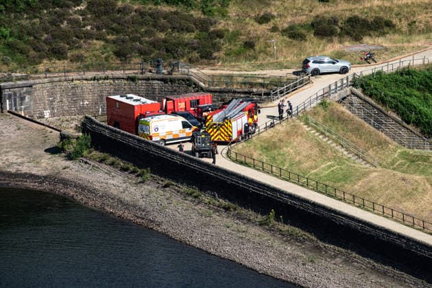Emergency vehicles at the scene of smouldering moorland close to Dove Stone Reservoir in Greater Manchester on 13 July 2026. Greater Manchester Police have arrested a woman in connection with a large moorland fire at Dove Stone Reservoir in Greenfield. The blaze, burning since Saturday, is under active investigation, with officers following leads regarding reports of fireworks nearby. The 20-year-old suspect remains in custody as the cause of the fire is yet to be officially determined. Oldham Greater Manchester England Dovestone Reservoir  Copyright: xMattxWilkinsonx