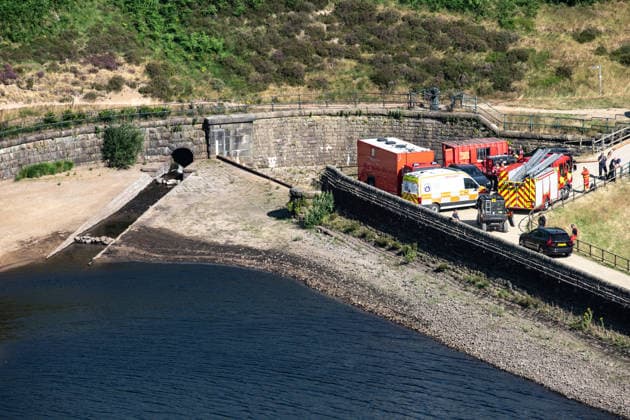 Emergency vehicles at the scene of smouldering moorland close to Dove Stone Reservoir in Greater Manchester on 13 July 2026. Greater Manchester Police have arrested a woman in connection with a large moorland fire at Dove Stone Reservoir in Greenfield. The blaze, burning since Saturday, is under active investigation, with officers following leads regarding reports of fireworks nearby. The 20-year-old suspect remains in custody as the cause of the fire is yet to be officially determined. Oldham Greater Manchester England Dovestone Reservoir  Copyright: xMattxWilkinsonx