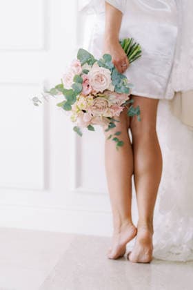 Braut mit einem pastellfarbenen Rosenstrauß in einem weißen Raum A bride in a white satin robe stands barefoot on tiptoe, holding a bouquet of pastel roses and eucalyptus leaves against a white paneled wall. (License=RF) ,model released, Symbolfoto Copyright: xZoonar.com Nadtochiy.comx 25324663 ,model released, Symbolfoto ,property released