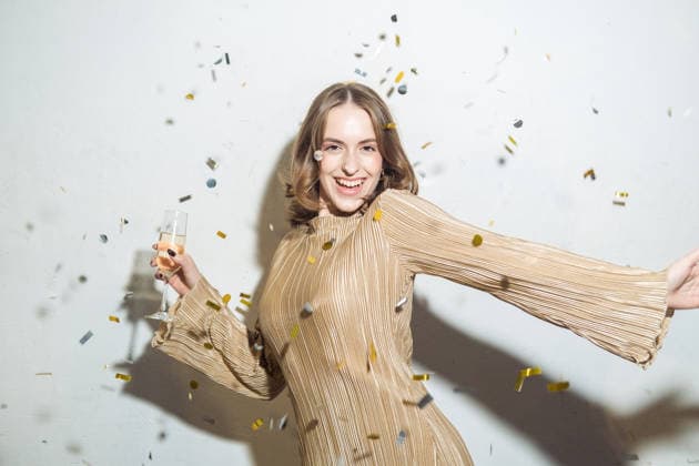 Eine fröhliche junge Frau mit einem Glas Champagner, während goldenes Konfetti durch die Luft wirbelt. Feier, Party, Spaß. A happy young woman with a glass of champagne and golden confetti flying in the air. (License=RF) ,model released, Symbolfoto Copyright: xZoonar.com RaisaxKanarevax 25330289 ,model released, Symbolfoto ,property released