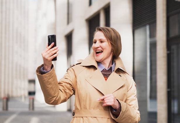 Eine reife, lächelnde Frau in einem beigen Mantel macht an einem Frühlingstag in einer städtischen Umgebung ein Selfie. A mature woman in a beige coat takes a selfie in an urban location on a spring day. (License=RF) ,model released, Symbolfoto Copyright: xZoonar.com RaisaxKanarevax 25330470 ,model released, Symbolfoto ,property released