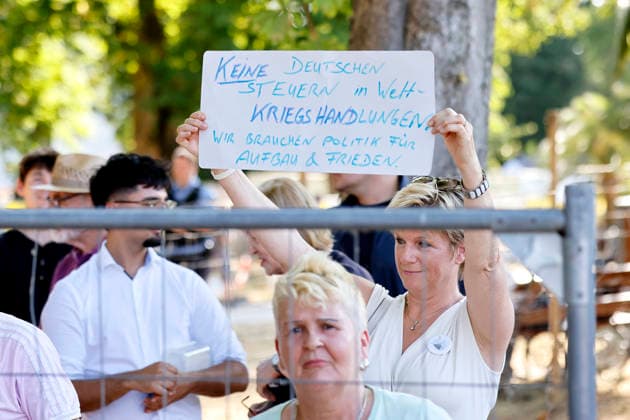 Eine Demonstrantin fordert mit einem Schild weniger Steuern für Kriegshandlungen beim Besuch von Bundeskanzler Friedrich Merz (CDU) auf dem Baustelle im Kurpark anlässlich des fünften Jahrestag der Flutkatastrophe im Ahrtal. Die Flut in der Nacht vom 14. auf den 15. Juli 2021 in Rheinland-Pfalz und Nordrhein-Westfalen war eine der verheerendsten Naturkatastrophen in der jüngeren deutschen Geschichte. Bad Neuenahr-Ahrweiler, 14.07.2026 Rheinland-Pfalz Deutschland *** A protester holds up a sign calling for lower taxes on military operations during a visit by Federal Chancellor Friedrich Merz (CDU) to the construction site in the Kurpark on the occasion of the fifth anniversary of the flood disaster in the Ahr Valley. The flood that occur Copyright: xChristophxHardtx