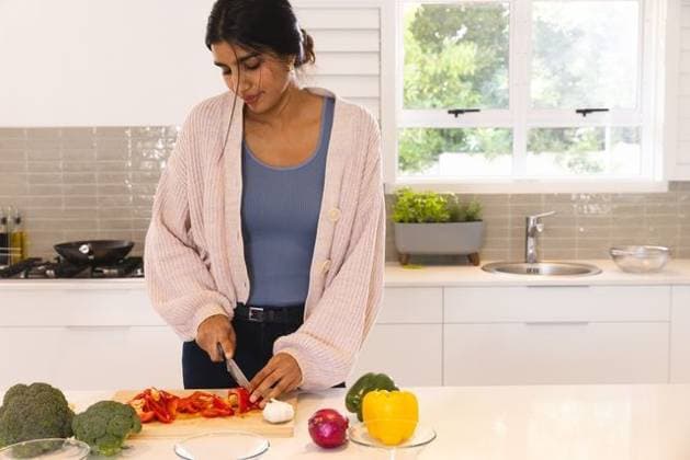 Asian woman standing at kitchen island, slicing red bell pepper on wooden cutting board, model released, property released, 03.10.2024 06:00:00, 6536754 Copyright: xIDS-250920_2xcreatorid:x0x 6536754