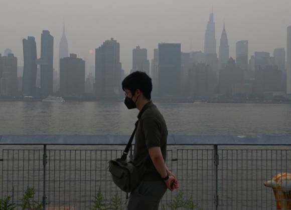 July 16, 2026, New York, New York, USA: July 16, 2026 - New York, NY, USA - Masked man walking with New York City midtown skyline and the Empire State Building seen across the East River which is covered by smoke coming from the ongoing Canadian wildfires. New Yorkers out with their families, friends, and pets go about their lives as they navigate the smoked filled air. (Andrea RENAULT Zuma Press) New York USA - ZUMAg115 20260716_faf_g115_039 Copyright: xAndreaxRenaultx