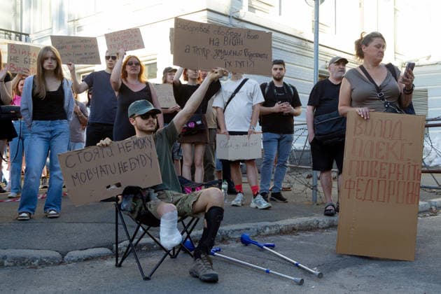 A veteran with an amputated leg holds placards while sitting in a camping chair with crutches lying nearby during a protest action against the dismissal of Ukrainian Defence Minister Mykhailo Fedorov in Ivana Franka Square in the evening on the second day of rallies, Kyiv, Ukraine, July 17, 2026. (Photo by Kyrylo Chubotin Ukrinform) Protest action against dismissal of Mykhailo Fedorov goes on in Kyiv  Copyright: xKyryloxChubotinx