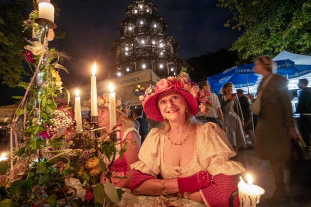 Kocherlball am Chinesischen Turm, Biertrinken bei Kerzenschein um 4:10 Uhr, München, 19. Juli 2026 Deutschland, München, 19. Juli 2026, Biertrinken bei Kerzenschein um 4:15 Uhr, traditioneller Kocherlball am Chinesischen Turm, Englischer Garten, manche Besucher sind schon um 3 Uhr früh im Biergarten, um noch einen Platz zu ergattern, Hier: Barbara Schaller aus dem Landkreis Dachau trägt einen einfallsreichen Hut mit Blumendeko, die Menschen trinken ein Bier, essen eine Brotzeit, tragen Tracht, Tradition entstand im 19. Jahrhundert, als Hauspersonal, Dienstboten und KöchInnen in den frühen Morgenstunden vor Dienstbeginn gefeiert und getanzt haben, Tradition wurde ab 1989 wiederbelebt, traditionell am 3. Sonntag im Juli, feiern, Traditi