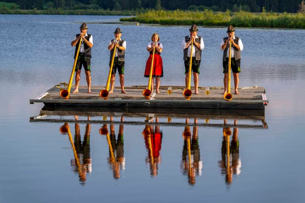21.07.2026, Der Moorsee Elbsee bei Aitrang im Allgäu, am Elbseerestaurant spielen die Günztaler Alphornbläser aus Markt Rettenbach (Unterallgäu) auf einem Floß heimatliche Klänge in idyllischer Umgebung. 21.07.2026, Elbsee bei Aitrang 21.07.2026, Elbsee bei Aitrang *** July 21, 2026, The Elbsee, a moorland lake near Aitrang in the Allgäu region; at the Elbsee Restaurant, the Günztaler Alphorn Players from Markt Rettenbach in the Unterallgäu region play traditional tunes on a raft in an idyllic setting July 21, 2026, Elbsee near Aitrang, July 21, 2026; Elbsee near Aitrang