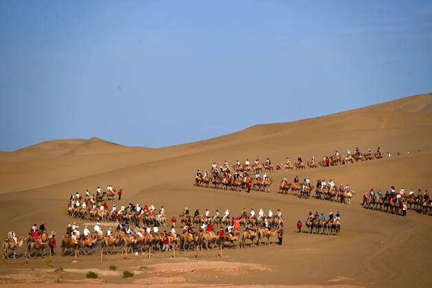 DUNHUANG, CHINA - JULY 19: Tourists ride camels at the Mingsha Mountain and Crescent Lake scenic area on July 19, 2026 in Dunhuang, Gansu Province of China. The site is a popular desert destination known for its sand dunes and crescent-shaped lake.  Copyright: xVCGx 111655630013