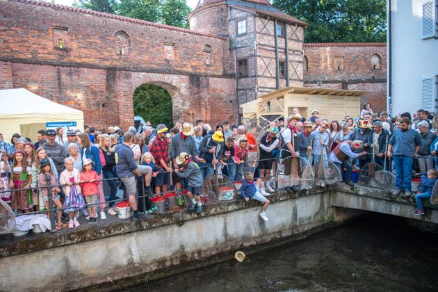Ein Blick auf das traditionelle Bachausfischen während des Fischertags in Memmingen. Zahlreiche Fischer in teils historischer Kleidung waten durch den Stadtbach, um Fische zu fangen. Dicht gedrängt stehen Zuschauer am Ufer und verfolgen das Spektakel, das jährlich tausende Besucher anzieht. Im Hintergrund sind die historischen Mauern der Stadt zu sehen. Der Memminger Fischertag ist eines der ältesten und bekanntesten Volksfeste in Bayern. Memmingen Bayern Deutschland *** A look at the traditional stream fishing during Fishermen’s Day in Memmingen. Numerous fishermen, some in historical attire, wade through the town stream to catch fish. Spectators stand crowded together on the bank, watching the spectacle, which attracts thousands of