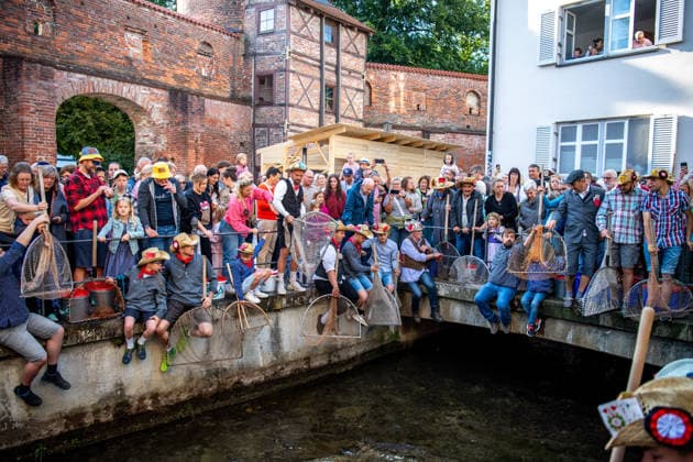 Ein Blick auf das traditionelle Bachausfischen während des Fischertags in Memmingen. Zahlreiche Fischer in teils historischer Kleidung waten durch den Stadtbach, um Fische zu fangen. Dicht gedrängt stehen Zuschauer am Ufer und verfolgen das Spektakel, das jährlich tausende Besucher anzieht. Im Hintergrund sind die historischen Mauern der Stadt zu sehen. Der Memminger Fischertag ist eines der ältesten und bekanntesten Volksfeste in Bayern. Memmingen Bayern Deutschland *** A look at the traditional stream fishing during Fishermen’s Day in Memmingen. Numerous fishermen, some in historical attire, wade through the town stream to catch fish. Spectators stand crowded together on the bank, watching the spectacle, which attracts thousands of