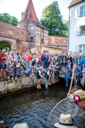 Ein Blick auf das traditionelle Bachausfischen während des Fischertags in Memmingen. Zahlreiche Fischer in teils historischer Kleidung waten durch den Stadtbach, um Fische zu fangen. Dicht gedrängt stehen Zuschauer am Ufer und verfolgen das Spektakel, das jährlich tausende Besucher anzieht. Im Hintergrund sind die historischen Mauern der Stadt zu sehen. Der Memminger Fischertag ist eines der ältesten und bekanntesten Volksfeste in Bayern. Memmingen Bayern Deutschland *** A look at the traditional stream fishing during Fishermen’s Day in Memmingen. Numerous fishermen, some in historical attire, wade through the town stream to catch fish. Spectators stand crowded together on the bank, watching the spectacle, which attracts thousands of