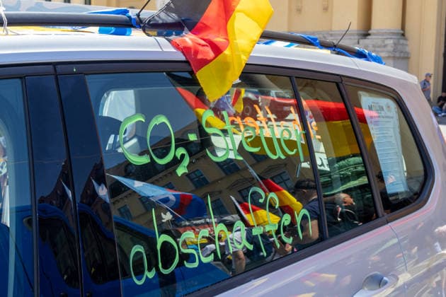 Munich, Bavaria, Germany July 25, 2026: Protesters demonstrate in downtown Munich against Chancellor Friedrich Merz (CDU) and the federal government™s policies. The rally is directed, among other things, against the government™s economic and social policies. A car with a German flag and the words Abolish the CO2 tax written on the windshield *** Teilnehmer demonstrieren in der Münchner Innenstadt gegen Bundeskanzler Friedrich Merz (CDU) und die Politik der Bundesregierung. Die Kundgebung richtet sich unter anderem gegen die Regierungs- und Sozialpolitik. Ein Auto, KFZ, mit Deutschlandfahne und der Aufschrift auf der Scheibe: CO2 Steuer abschaffen