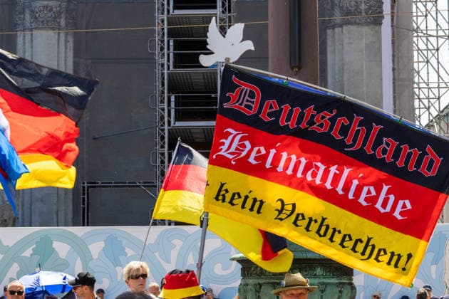 Munich, Bavaria, Germany - July 25, 2026: Protesters demonstrate in downtown Munich against Chancellor Friedrich Merz (CDU) and the federal government™s policies. The rally is directed, among other things, against the government™s policies and social policies. Banner with the inscription: Germany, love for one™s homeland is not a crime! *** Teilnehmer demonstrieren in der Münchner Innenstadt gegen Bundeskanzler Friedrich Merz (CDU) und die Politik der Bundesregierung. Die Kundgebung richtet sich unter anderem gegen die Regierungs- und Sozialpolitik.Fahne bzw. Flagge mit Aufschrift: Deutschland, Heimatliebe ist kein Verbrechen!
