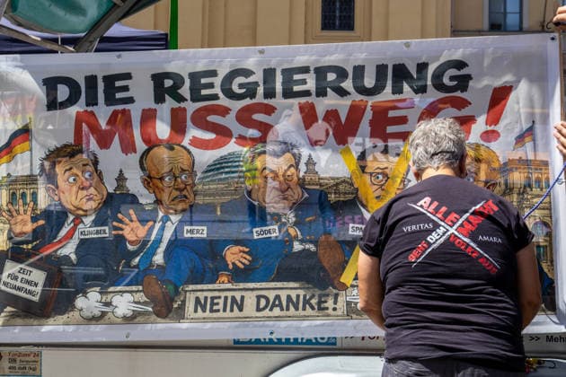 Munich, Bavaria, Germany - July 25, 2026: Protesters demonstrate in downtown Munich against Chancellor Friedrich Merz (CDU) and the federal government s policies. The rally is directed, among other things, against the government™s policies and social policies. A banner reads: THE GOVERNMENT MUST GO! with illustrations of Lars Klingbeil (SPD), Friedrich Merz (CDU), Markus Söder (CSU), and Jens Spahn (CDU) crossed out, and Daniel Günther (CDU) *** Teilnehmer demonstrieren in der Münchner Innenstadt gegen Bundeskanzler Friedrich Merz (CDU) und die Politik der Bundesregierung. Die Kundgebung richtet sich unter anderem gegen die Regierungs- und Sozialpolitik. Banner mit Aufschrift: DIE REGIERUNG MUSS WEG! mit Illustrationen von Lars K
