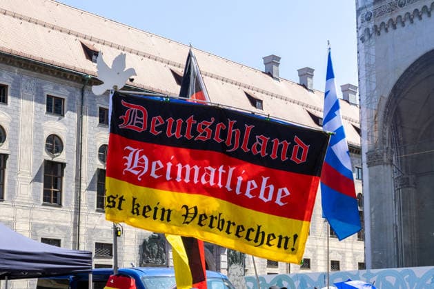 Munich, Bavaria, Germany - July 25, 2026: Protesters demonstrate in downtown Munich against Chancellor Friedrich Merz (CDU) and the federal government™s policies. The rally is directed, among other things, against the government™s policies and social policies. Banner with the inscription: Germany, love for one™s homeland is not a crime! *** Teilnehmer demonstrieren in der Münchner Innenstadt gegen Bundeskanzler Friedrich Merz (CDU) und die Politik der Bundesregierung. Die Kundgebung richtet sich unter anderem gegen die Regierungs- und Sozialpolitik.Fahne bzw. Flagge mit Aufschrift: Deutschland, Heimatliebe ist kein Verbrechen!