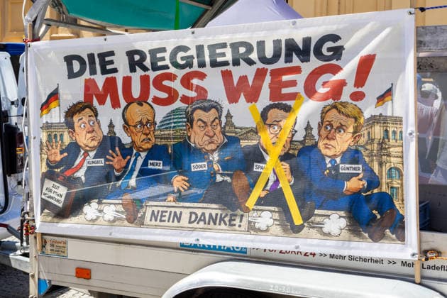 Munich, Bavaria, Germany - July 25, 2026: Protesters demonstrate in downtown Munich against Chancellor Friedrich Merz (CDU) and the federal government s policies. The rally is directed, among other things, against the government™s policies and social policies. A banner reads: THE GOVERNMENT MUST GO! with illustrations of Lars Klingbeil (SPD), Friedrich Merz (CDU), Markus Söder (CSU), and Jens Spahn (CDU) crossed out, and Daniel Günther (CDU) *** Teilnehmer demonstrieren in der Münchner Innenstadt gegen Bundeskanzler Friedrich Merz (CDU) und die Politik der Bundesregierung. Die Kundgebung richtet sich unter anderem gegen die Regierungs- und Sozialpolitik. Banner mit Aufschrift: DIE REGIERUNG MUSS WEG! mit Illustrationen von Lars K