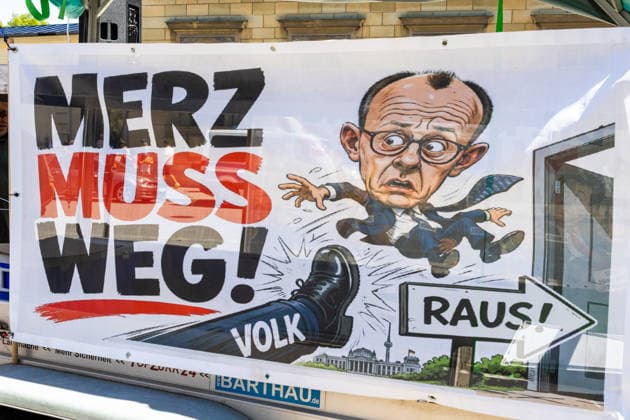 Munich, Bavaria, Germany July 25, 2026: Protesters demonstrate in downtown Munich against Chancellor Friedrich Merz (CDU) and the federal government™s policies. Among other things, the rally is directed against the government™s policies and social policies. A poster reads: MERZ MUST GO! and features an illustration of a foot kicking the chancellor with the caption: PEOPLE, and an arrow pointing through a door with the caption: GET OUT! *** Teilnehmer demonstrieren in der Münchner Innenstadt gegen Bundeskanzler Friedrich Merz (CDU) und die Politik der Bundesregierung. Die Kundgebung richtet sich unter anderem gegen die Regierungs- und Sozialpolitik. Plakat mit Aufschrift: MERZ MUSS WEG! und einer Illustration mit e