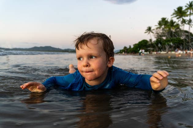 Young boy in blue rash guard floats in shallow ocean water Tamarindo, Guanacaste Province, Costa Rica CR_XICZ260724-2074380-01 ,model released, Symbolfoto ,property released