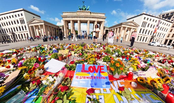 Zahlreiche Menschen haben vor dem Brandenburger Tor Blumen, Kerzen, Regenbogenfahnen niedergelegt und trauern um die Opfer des CSD-Anschlags, Berlin, 27. Juli 2026 Deutschland, Berlin, 27. Juli 2026, Gedenkort für die Opfer des CSD-Anschlags vor dem Brandenburger Tor, zahlreiche Menschen haben Blumen, Kerzen, Regenbogenfahnen niedergelegt, einen Erinnerungsort geschaffen, im Mittelpunkt liegt ein handgemaltes Schild mit der Aufschrift: Love is stronger than hate, das Blumenmeer setzt ein sichtbares Zeichen gegen Hass und Gewalt, Szene auf dem Pariser Platz am Montagmorgen um 10 Uhr, 36 Stunden nach dem islamistischen Terroranschlag im Tiergarten, bei dem ein Mensch starb und weitere teils schwer verletzt wurden, *** Numerous people have la