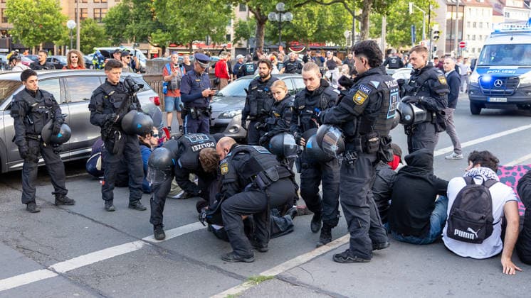 Montagsdemo Team Menschenrechte mit Gegendemonstration und Blockaden, Nürnberg, 27.07.2026 Mehrere Polizeibeamte in Schutzausrüstung lösen eine Sitzblockade auf und nehmen Personen zu Boden fest. Umstehende Personen beobachten den Einsatz, im Hintergrund steht ein Polizeifahrzeug bereit. Nürnberg Bayern Deutschland *** Monday Demonstration: Human Rights Team Holds Counter-Demonstration and Sets Up Blockades, Nuremberg, July 27, 2026 Several police officers in protective gear break up a sit-in and subdue individuals on the ground. Bystanders watch the operation; a police vehicle stands by in the background. Nuremberg, Bavaria, Germany 20260727-286A3105-M4000