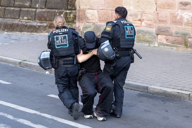 Montagsdemo Team Menschenrechte mit Gegendemonstration und Blockaden, Nürnberg, 27.07.2026 Zwei Polizeibeamte in Schutzausrüstung führen einen Gegendemonstranten von der Blockade weg. Der Mann wird von beiden Seiten an den Armen gehalten und abgeführt. Nürnberg Bayern Deutschland *** Monday Demonstration: Human Rights Team Holds Counter-Demonstration and Roadblocks, Nuremberg, July 27, 2026. Two police officers in protective gear lead a counter-demonstrator away from the roadblock. The man is held by the arms on both sides and escorted away. Nuremberg, Bavaria, Germany 20260727-286A3138-M4000