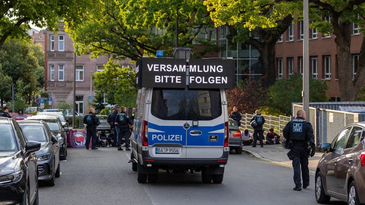 Montagsdemo Team Menschenrechte mit Gegendemonstration und Blockaden, Nürnberg, 27.07.2026 Ein Einsatzfahrzeug der Polizei mit Leuchtschrift-Anzeige Versammlung bitte folgen steht auf einer Straße, umgeben von Einsatzkräften. Am Straßenrand sitzen und stehen mehrere Personen im Rahmen einer Blockade, Polizeibeamte sichern die Situation ab. Nürnberg Bayern Deutschland *** Monday Demonstration: Human Rights Team with a counter-demonstration and roadblocks, Nuremberg, July 27, 2026 A police emergency vehicle with a neon sign reading Please follow the procession is parked on a street, surrounded by law enforcement officers. Several people are sitting and standing at the roadside as part of a blockade; police officers are securing the 20260727-6V2A0248-M4000