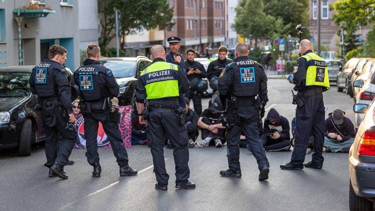 Montagsdemo Team Menschenrechte mit Gegendemonstration und Blockaden, Nürnberg, 27.07.2026 Mehrere Polizeibeamte in Einsatzkleidung sichern eine Straßenblockade in der oberen Turnstraße, während Sitzblockierer auf dem Asphalt sitzen. Ein Beamter der Polizeikommunikation steht im Vordergrund, im Hintergrund werden weitere Personen von Einsatzkräften begleitet. Nürnberg Bayern Deutschland *** Monday Demonstration: Human Rights Team with a counter-demonstration and roadblocks, Nuremberg, July 27, 2026 Several police officers in tactical gear secure a roadblock on Obere Turnstraße, while sit-in protesters sit on the asphalt. A police communications officer stands in the foreground; in the background, other individuals are being escorte 20260727-6V2A0259-M4000