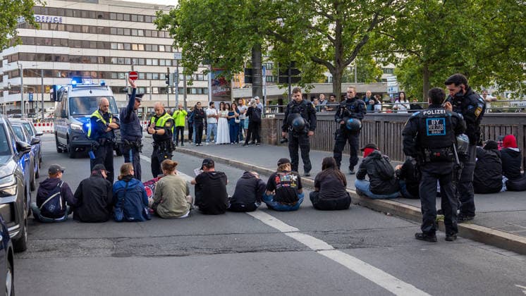 Montagsdemo Team Menschenrechte mit Gegendemonstration und Blockaden, Nürnberg, 27.07.2026 Mehrere Personen sitzen bei einer Straßenblockade am Ludwigstor die Verlängerung der Ludwigstraße, während zahlreiche Polizeikräfte in Einsatzuniform die Situation absichern. Ein Polizeibeamter gibt mit erhobener Hand Anweisungen, im Hintergrund beobachten Passanten das Geschehen. Einsatzfahrzeuge der Polizei stehen am Straßenrand bereit. Nürnberg Bayern Deutschland *** Monday Demonstration: Human Rights Team Holds Counter-Demonstration and Roadblocks, Nuremberg, July 27, 2026 Several people are sitting at a roadblock at Ludwigstor, the extension of Ludwigstraße, while numerous police officers in uniform secure the scene. A police officer g 20260727-286A3076-M4000