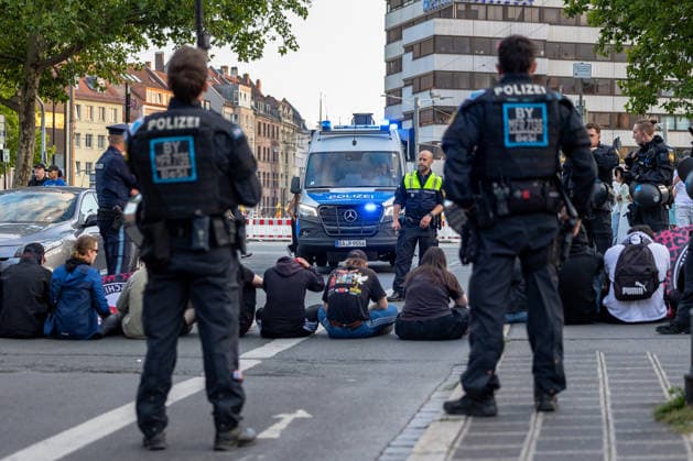 Montagsdemo Team Menschenrechte mit Gegendemonstration und Blockaden, Nürnberg, 27.07.2026 Polizeikräfte sichern eine Straßenblockade, bei der mehrere Personen sitzend die Fahrbahn besetzt halten. Ein Einsatzfahrzeug der Polizei mit Blaulicht steht auf der Straße, Beamte in Einsatzausrüstung beobachten die Situation. Nürnberg Bayern Deutschland *** Monday Demonstration: Human Rights Team with a counter-demonstration and roadblocks, Nuremberg, July 27, 2026 Police officers secure a roadblock where several people are sitting and occupying the roadway. A police emergency vehicle with its blue lights flashing is parked on the street; officers in riot gear are monitoring the situation. Nuremberg, Bavaria, Germany 20260727-6V2A0487-M4000