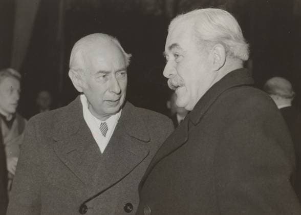 RECORD DATE NOT STATED Bundes President Prof. Heuss arrives in Hannover on November 30 for a state visit in Lower Saxony, Bundes President Prof. Heuss with Hinrich Kopf, photograph, photographer: International News Photos, unknown, 1949-12-02, paper, gelatin silver print, developing gelatin silver print on photo paper, height 131 mm x width 180 mm, Person, Theodor Heuss, meeting, Lower Saxony, Hannover., Two older men in dark overcoats stand facing each other in a black-and-white photograph, one shown in three-quarter profile with neatly combed light hair and a mustache, the other shown facing slightly toward him with slicked-back light hair and a visible patterned tie peeking from a white shirt; a blurred figure appears in the background on each side, and the sc  Copyright Penta Springs LCK260621_098425