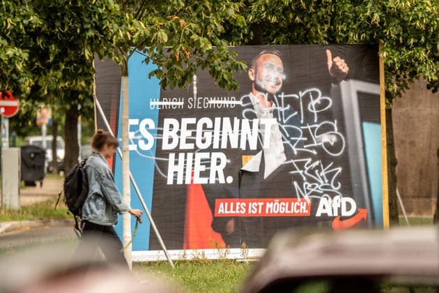 Von AfD-Gegnern übermaltes Wahlplakat mit Ulrich Siegmund, AfD-Spitzenkandidat bei den Landtagswahlen in Sachsen-Anhalt am 6. September, Wahkampf, Magdeburg, 28. Juli 2026 Deutschland, Magdeburg, 28. Juli 2026, beschädigtes Wahlplakat der AfD mit Ulrich Siegmund, AfD-Spitzenkandidat bei den Landtagswahlen in Sachsen-Anhalt am 6. September, Wahlslogan: Es beginnt hier, Alles ist möglich, Plakat im Magdeburger Stadtteil Cracau von AfD-Gegnern mit weißer Farbe beschmiert und teils übermalt, Passantin, rechtsextreme Landespartei, Wahlkampf, Politik, *** Election poster featuring Ulrich Siegmund, painted over by AfD opponents, AfD’s top candidate in the state elections in Saxony-Anhalt on September 6, election campaign, Magdeburg, July 28,