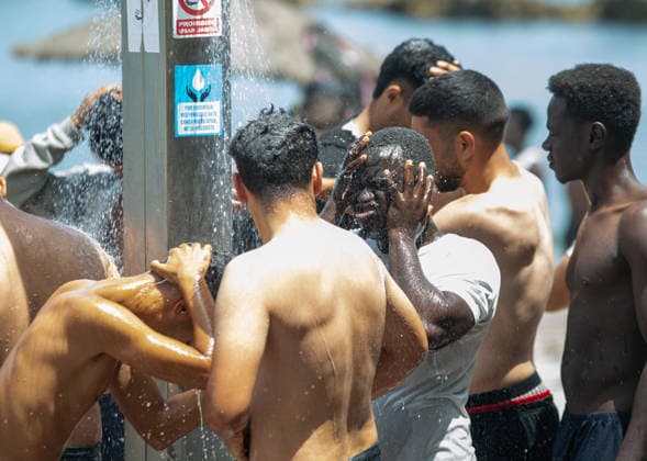 August 1, 2026, Ceuta, Ceuta, Spain: A group of migrants use beach showers near the Temporary Stay Centre for Immigrants Ceuta Spain - ZUMAd308 20260801_zsp_d308_085 Copyright: xJuanxCarlosxLucasx