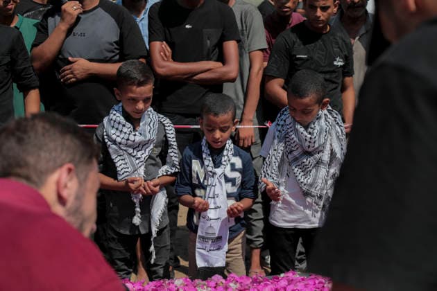Gaza City Mass Funeral August 3 2026 Mourners pray beside a flower-covered coffin as journalists document the scene during a mass funeral procession in the Al-Sabra neighborhood of Gaza City, Gaza Strip, on August 4, 2026. The remains of 112 members of the Abu Sharia and Al-Hasayneh families were recovered from the rubble of their home following an Israeli strike. Relatives stated the attack claimed the lives of more than 300 people. The bodies were buried at Al-Maamadani Cemetery as military operations continue across the territory. Gaza Gaza Strip Palestinian Territories Copyright: xEyadxAzamx