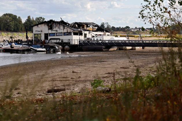 Das Sürther Bootshaus in Köln ist ausgebrannt. Am Tag nach dem Feuer ragt der verkohlte Dachstuhl in den Himmel, während das Restaurant unten wegen des Rekord-Niedrigwasser des Rhein fast auf dem Trockenen liegt. Die Brandursache für das Feuer in dem beliebten Ausflugslokal ist weiterhin unklar. Köln, 05.08.2026 NRW Deutschland *** The Sürther Bootshaus in Cologne has burned to the ground. The day after the fire, the charred roof truss towers toward the sky, while the restaurant below is nearly high and dry due to record-low water levels in the Rhine. The cause of the fire at the popular restaurant remains unclear. Cologne, August 5, 2026, North Rhine-Westphalia, Germany Copyright: xChristophxHardtx
