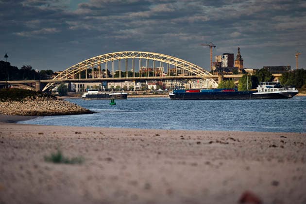 August 6, 2026, Nijmegen, Gelderland, Netherlands: Looking downstream near NIJMEGEN, cargo vessels sail along the WAAL past the iconic WAALBRUG and the city skyline, with a broad stretch of exposed sandy riverbed in the foreground. This main DUTCH branch of the RHINE is currently at historic low levels due to prolonged drought, forcing inland shipping to operate with sharply reduced loads and driving up transport costs. Credit : ZUMA Press Nijmegen Netherlands - ZUMAv145 20260806_zip_v145_003 Copyright: xNorbertxVoskensx