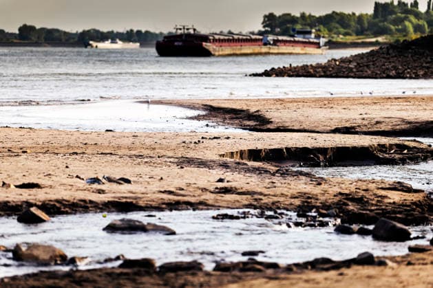 August 6, 2026, Nijmegen, Gelderland, Netherlands: The cracked and exposed riverbed of the WAAL near OOIJ stretches into the distance as a cargo barge sails upstream towards GERMANY. Prolonged drought has reduced water levels on this main Dutch branch of the RHINE to historic lows, forcing inland vessels to operate with sharply reduced loads and driving up transport costs. Credit : ZUMA Press Nijmegen Netherlands - ZUMAv145 20260806_zip_v145_007 Copyright: xNorbertxVoskensx