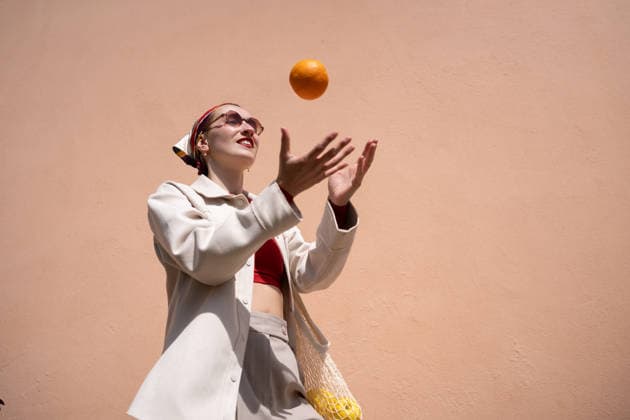 Woman catches orange against peach wall outdoors model released, Symbolfoto, ATSF00701