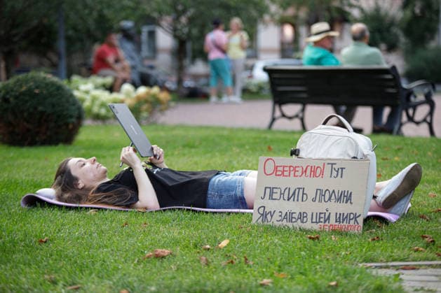 An activist lying on a sleeping pad on the lawn works on a tablet PC during a peaceful protest against the dismissal of Mykhailo Fedorov from the post of Ukraine’s Defence Minister in Ivana Franka Square outside the Ivan Franko National Academic Drama Theatre, close to the Office of the President, Kyiv, Ukraine, August 6, 2026. Large-scale cardboard rallies in support of former Defence Minister Mykhailo Fedorov have been held in Kyiv and other cities across Ukraine for 22 consecutive days. On 14 July 2026, the Ukrainian Parliament accepted the resignation of Prime Minister Yuliia Svyrydenko, leading to the resignation of the Cabinet. On 15 July 2026, President Volodymyr Zelenskyy dismissed Defence Minister Mykhailo Fedorov, sparking wides  Copyright: xMariannaxKotykx