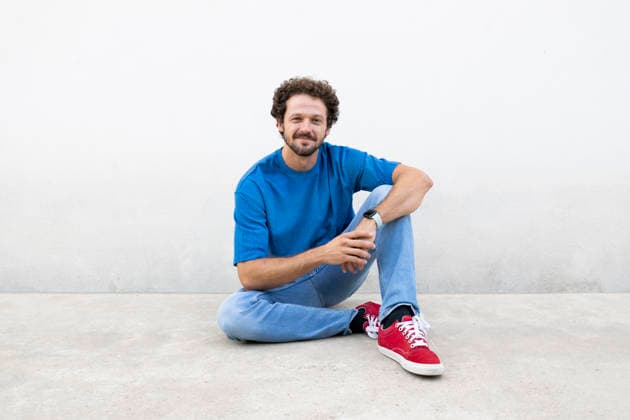 A smiling man sits on the floor against a white background model released, Symbolfoto, LMCF03141